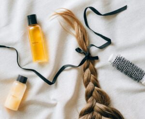 Flat lay of braided hair with shampoo bottles and brush on white fabric, conveying beauty and haircare themes.